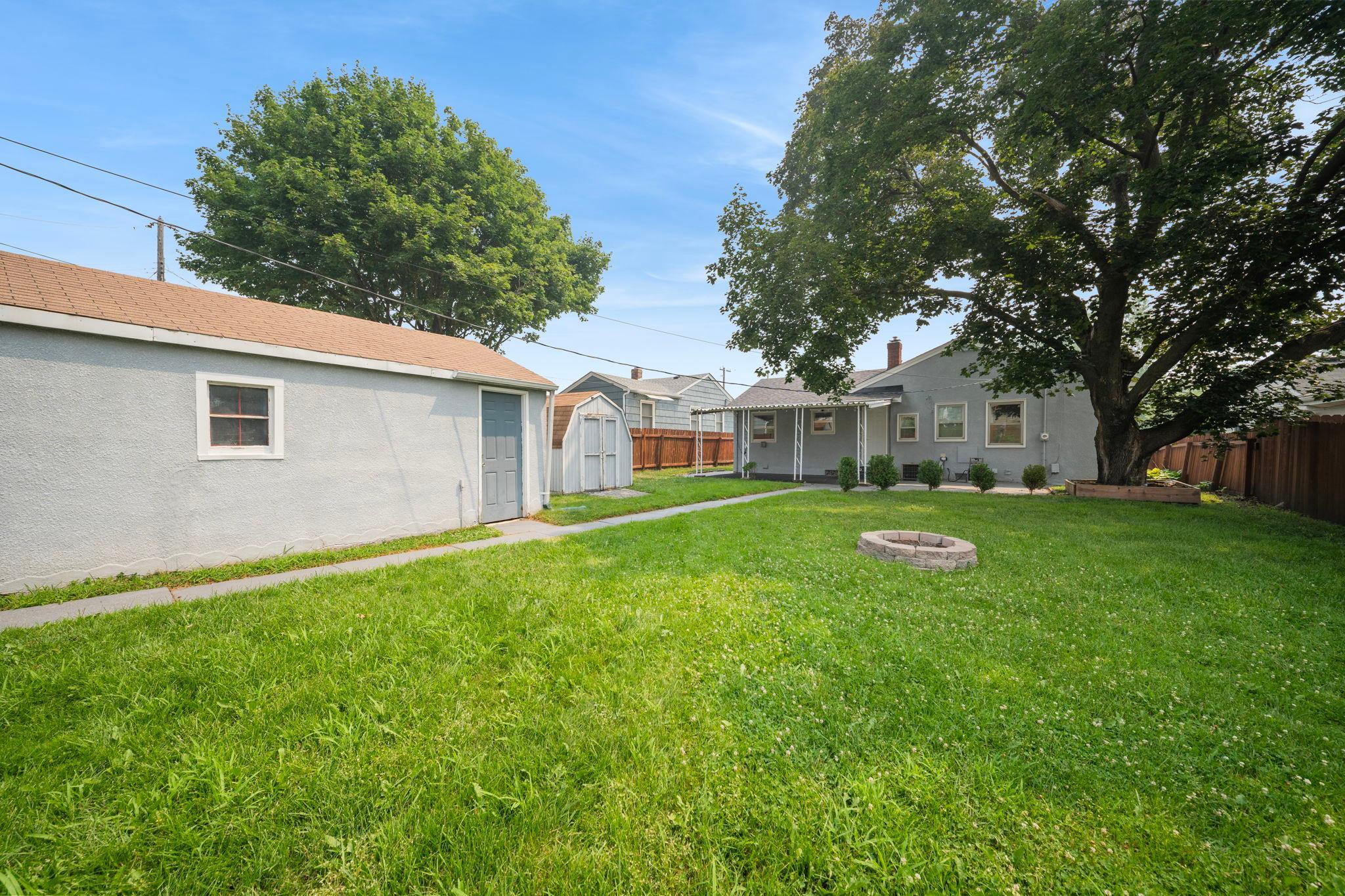 A backyard built for outdoor living, complete with a fire pit, storage shed, and mature shade trees. This is Twin Cities summer at its best.
