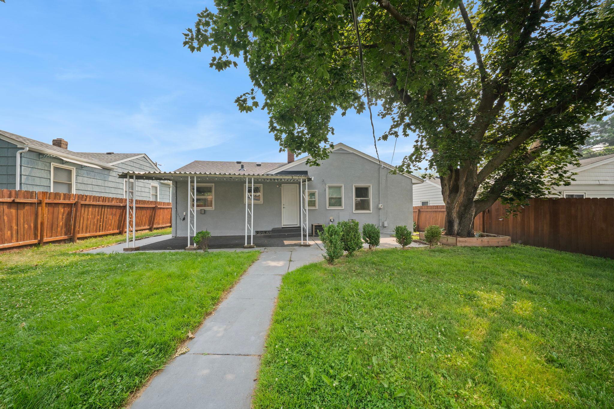 A shade tree towers over a fully fenced backyard. Kids, dogs, garden beds, this space holds every version of home life.