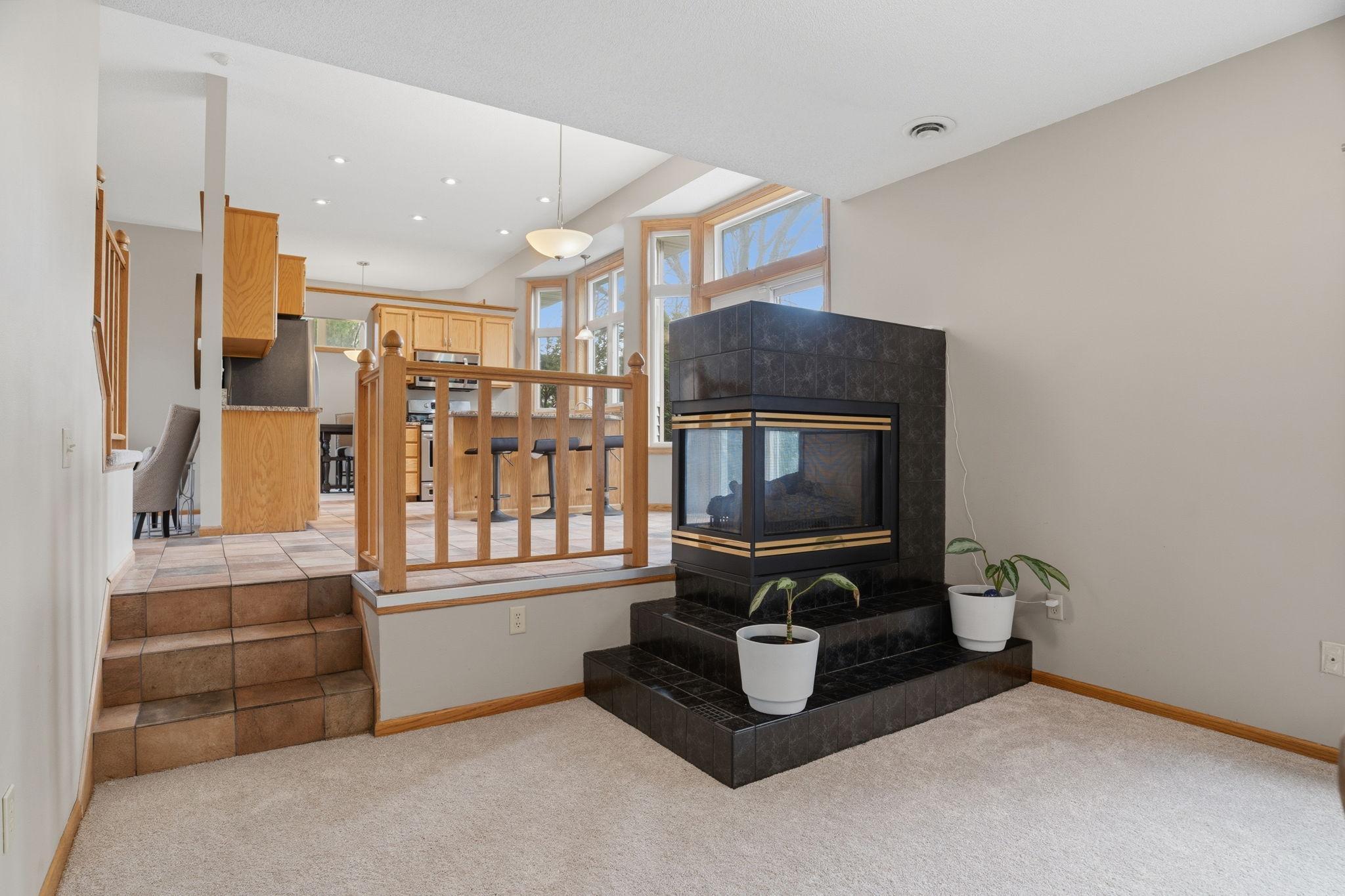 A striking two sided fireplace anchors this sunken family room, tiled steps rising to the kitchen above in an open layout built for everyday togetherness.
