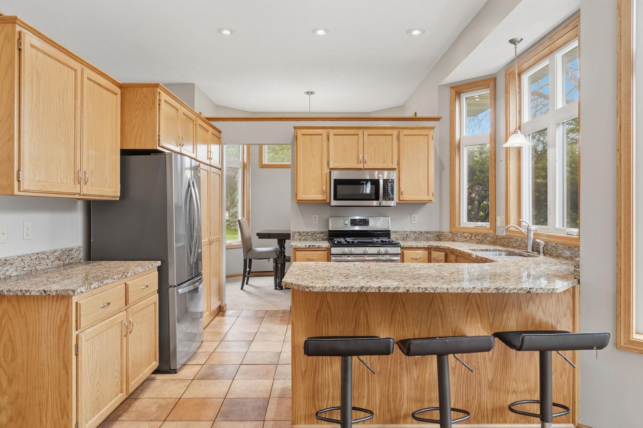 Sunlight pours through the bay window as granite counters wrap this open kitchen, gas range and peninsula seating flowing toward a bright dining nook beyond, made for cooking and gathering all at once.