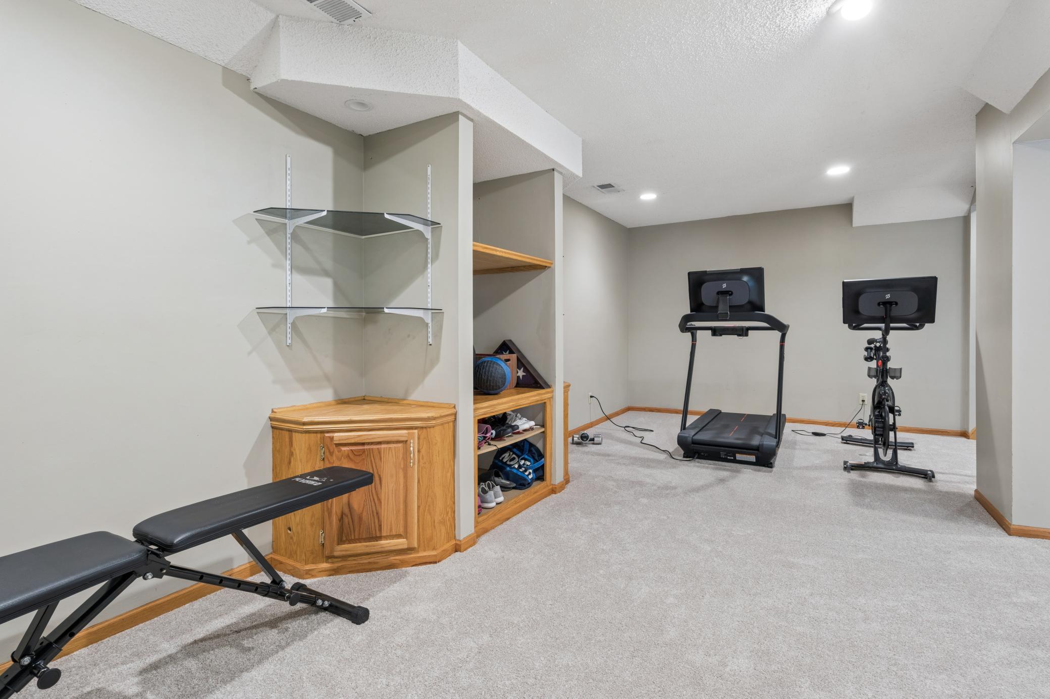 A cozy home gym that actually has everything. Treadmill, spin bike, weight bench, built-in shelving. The home gym zone is already set up and waiting.