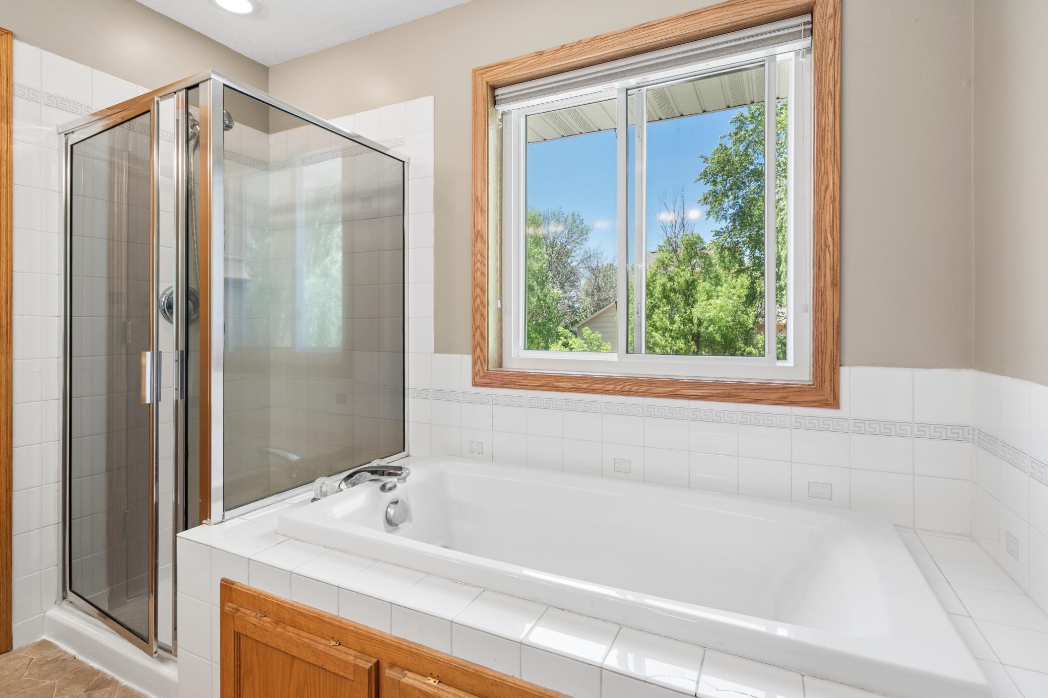 Soak or shower. The primary bath offers both without compromise. Tile surrounds the tub. The glass door opens to a full shower. Outside the window, the trees stand guard. Take your time.