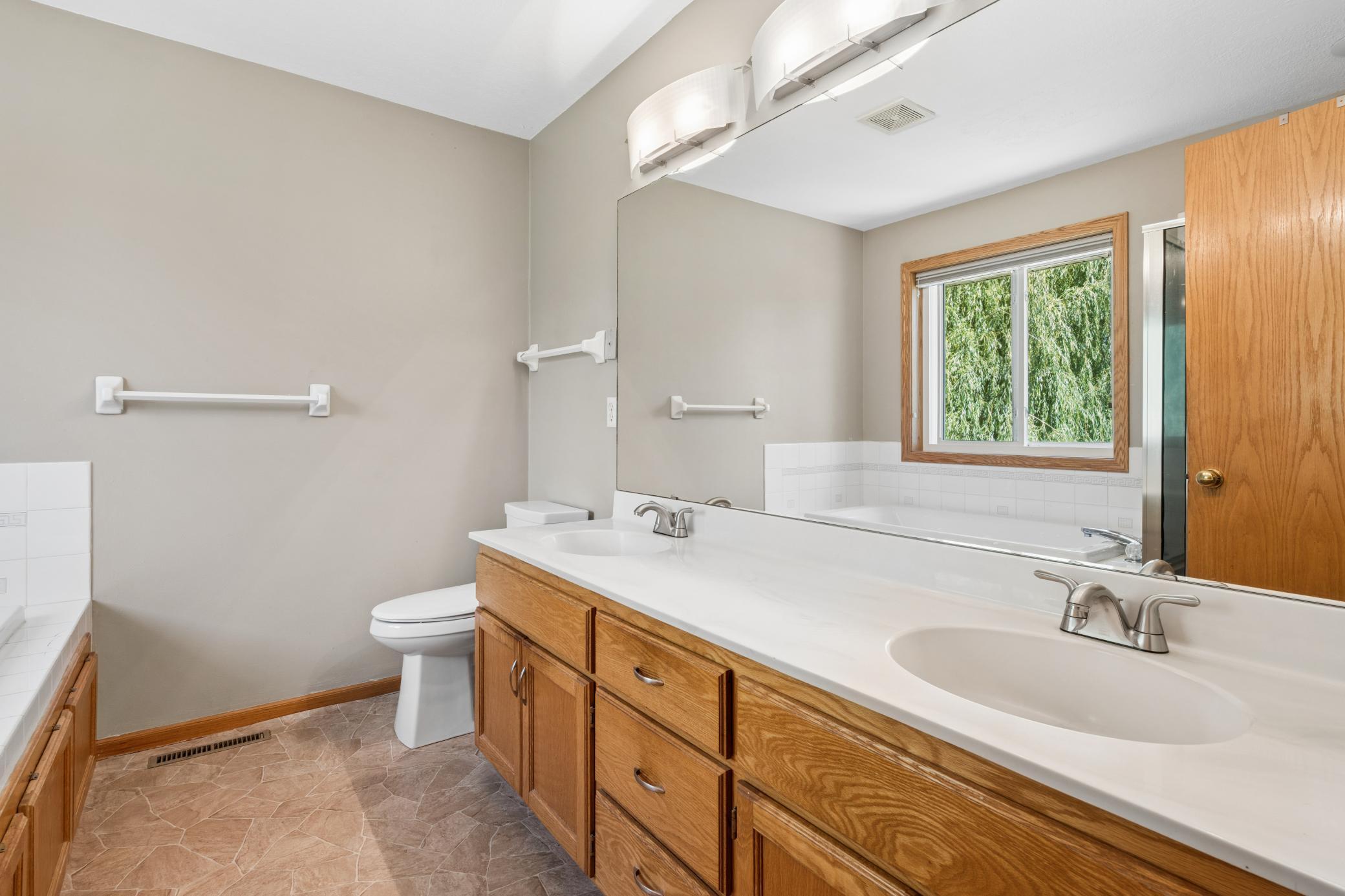 Owner suite private, full bathroom with double sinks. A soaking tub. A window framing the treetops. The primary bath doesn't rush you. Wide vanity, warm wood cabinetry, and enough room to start the day right.