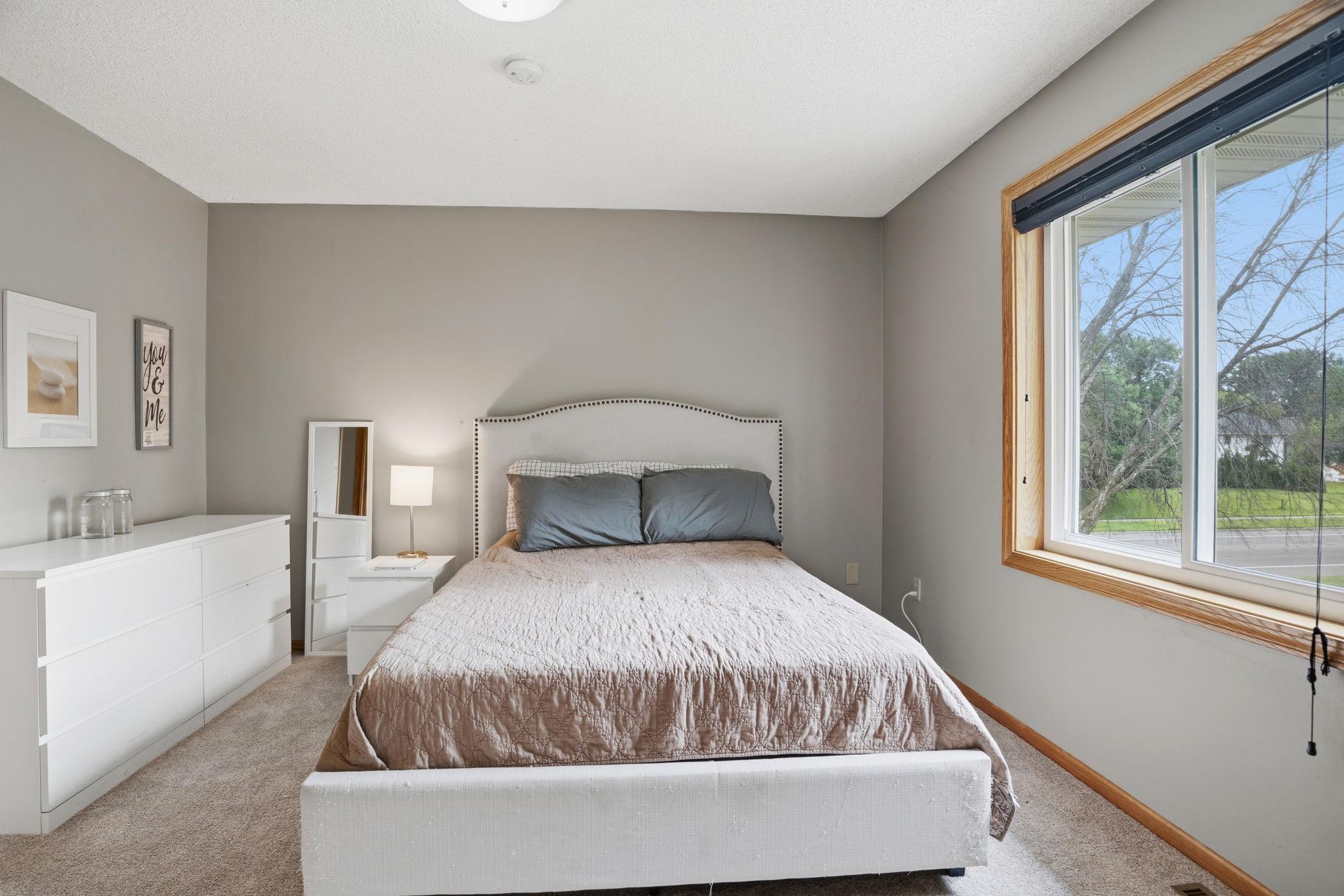 Natural light floods this spacious bedroom through its oversized window, neutral tones and plush carpet offering a calm canvas ready for any style.