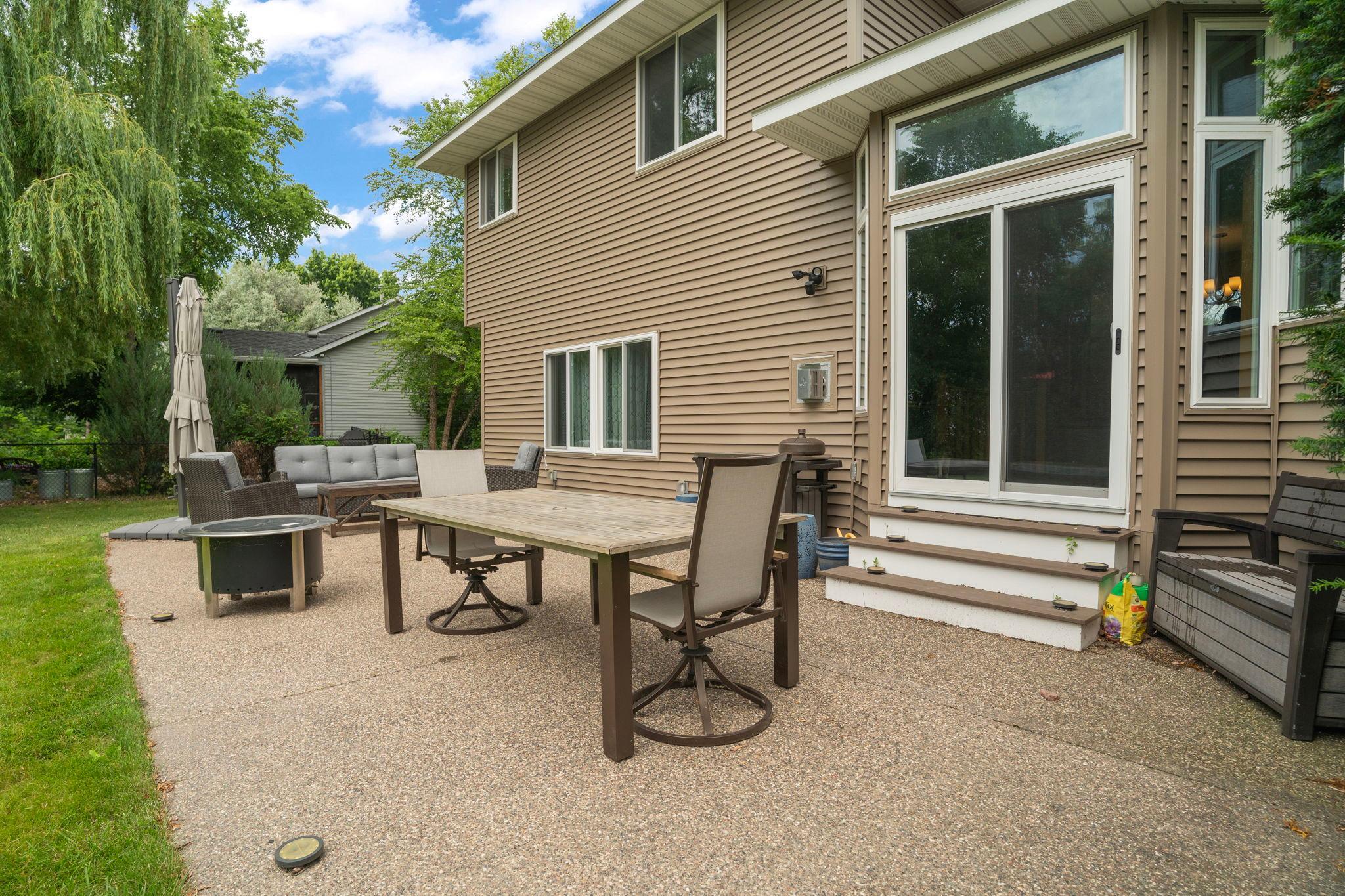 A wide patio steps right off the kitchen, willow branches swaying overhead and grass stretching beyond. Room for a crowd, a fire, a slow summer evening. Indoor living spills right outside.