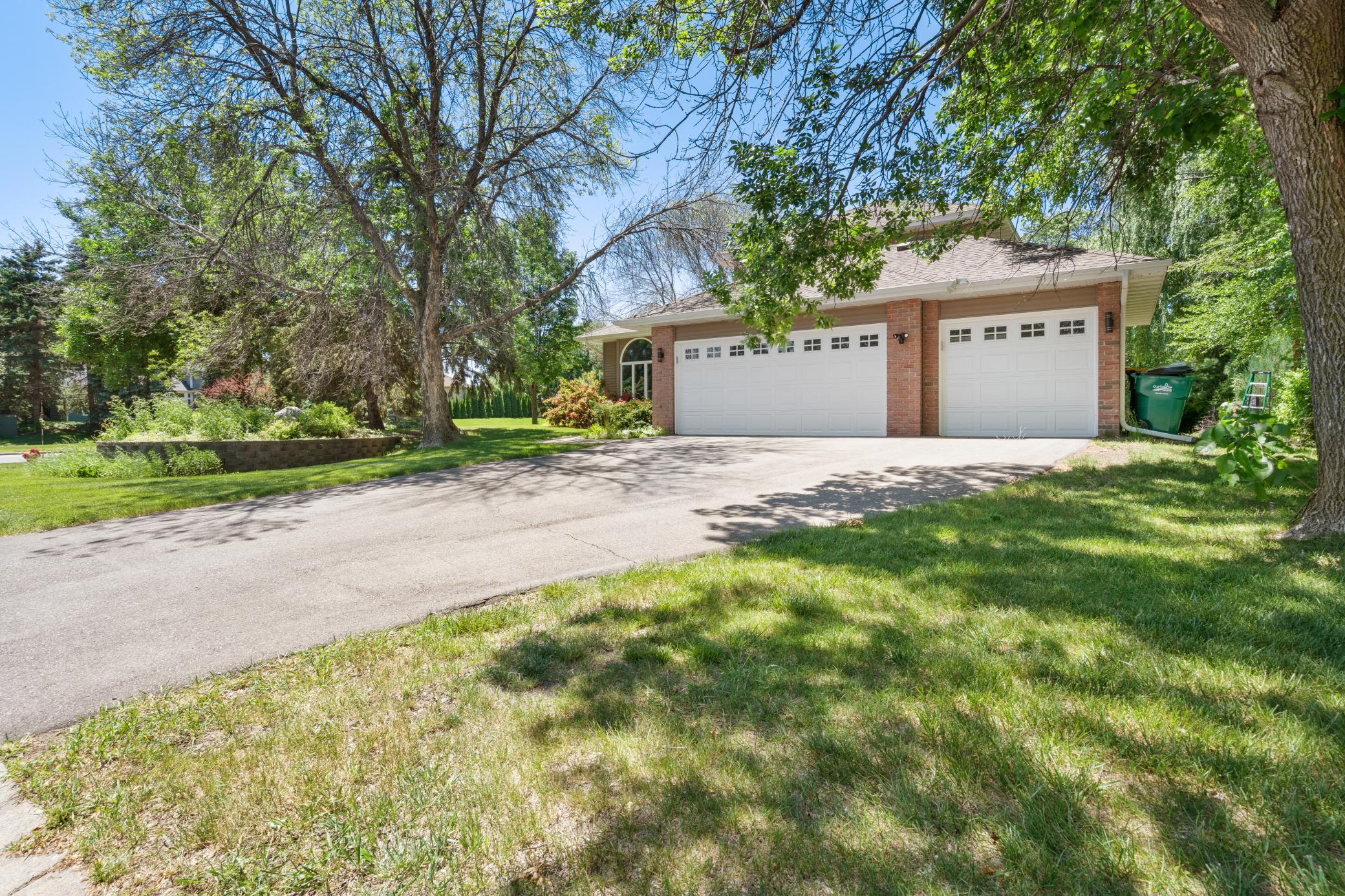Pull in and the lot opens up. The three-car garage runs wide. The trees close in on both sides. The corner lot gives you more yard than the neighbors and more privacy than you expected.
