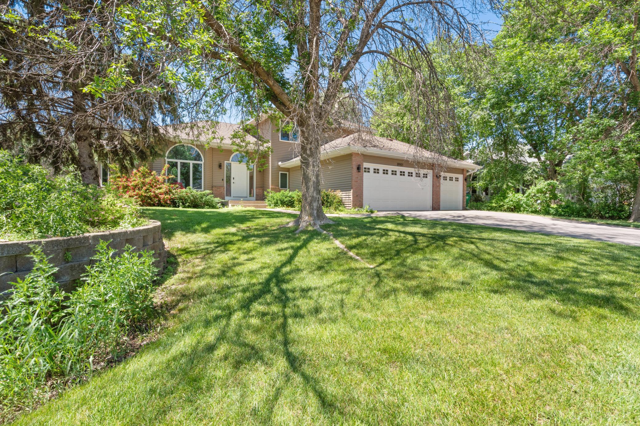 Mature trees casting long shadows across a lush corner lot. The stone retaining wall. The arched window catching the light. This is the home that makes people slow down when they drive by.