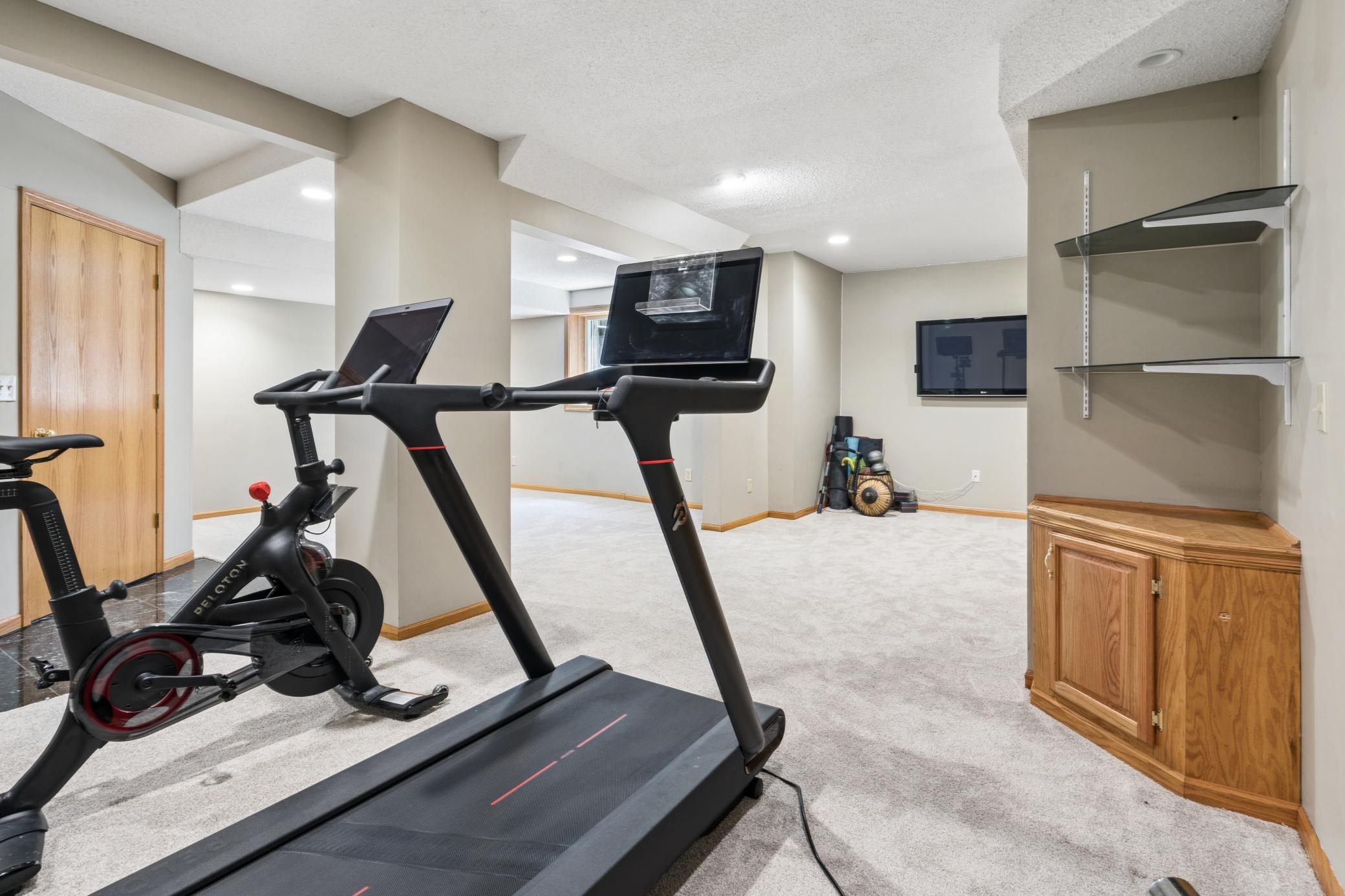 This lower level family room does double duty beautifully. The Peloton and treadmill claim their corner, the wall-mounted TV keeps you company, and the family room waits just beyond for when the workout is done.