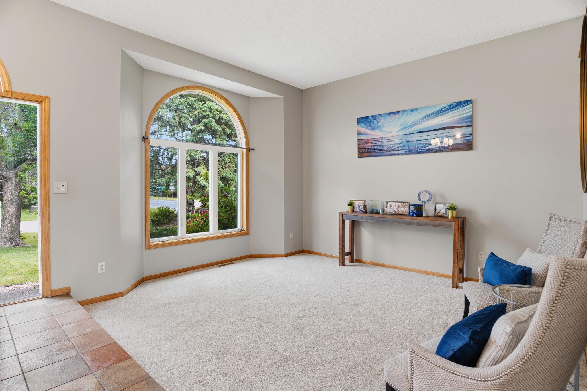 A dramatic arched window fills this formal living room with light, its soaring ceiling and plush carpet creating an airy, welcoming space just off the entry.