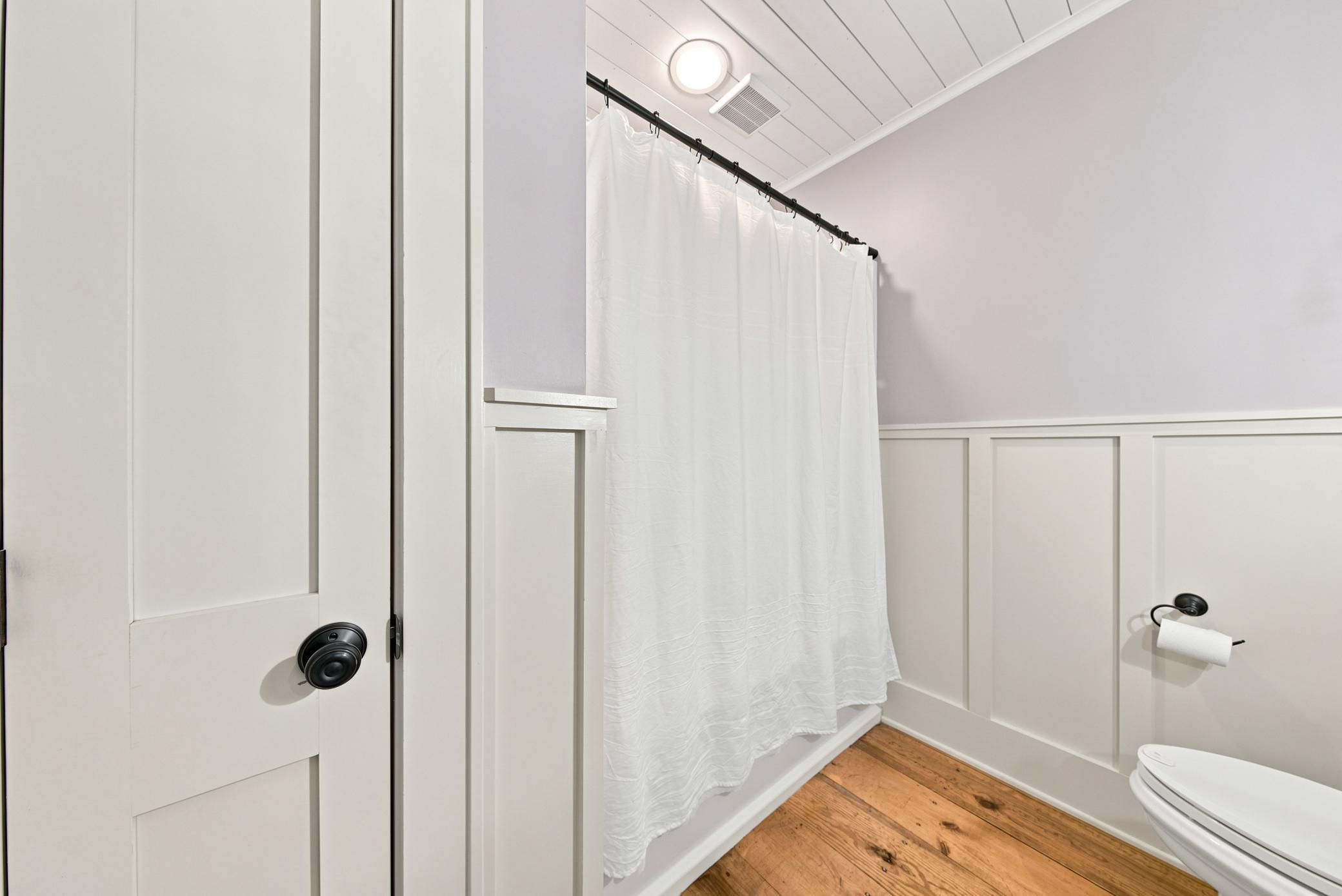 This charming farmhouse-style bathroom on main floor features elegant wainscoting, wide-plank wood floors, a classic pedestal sink, and custom modern light fixtures.