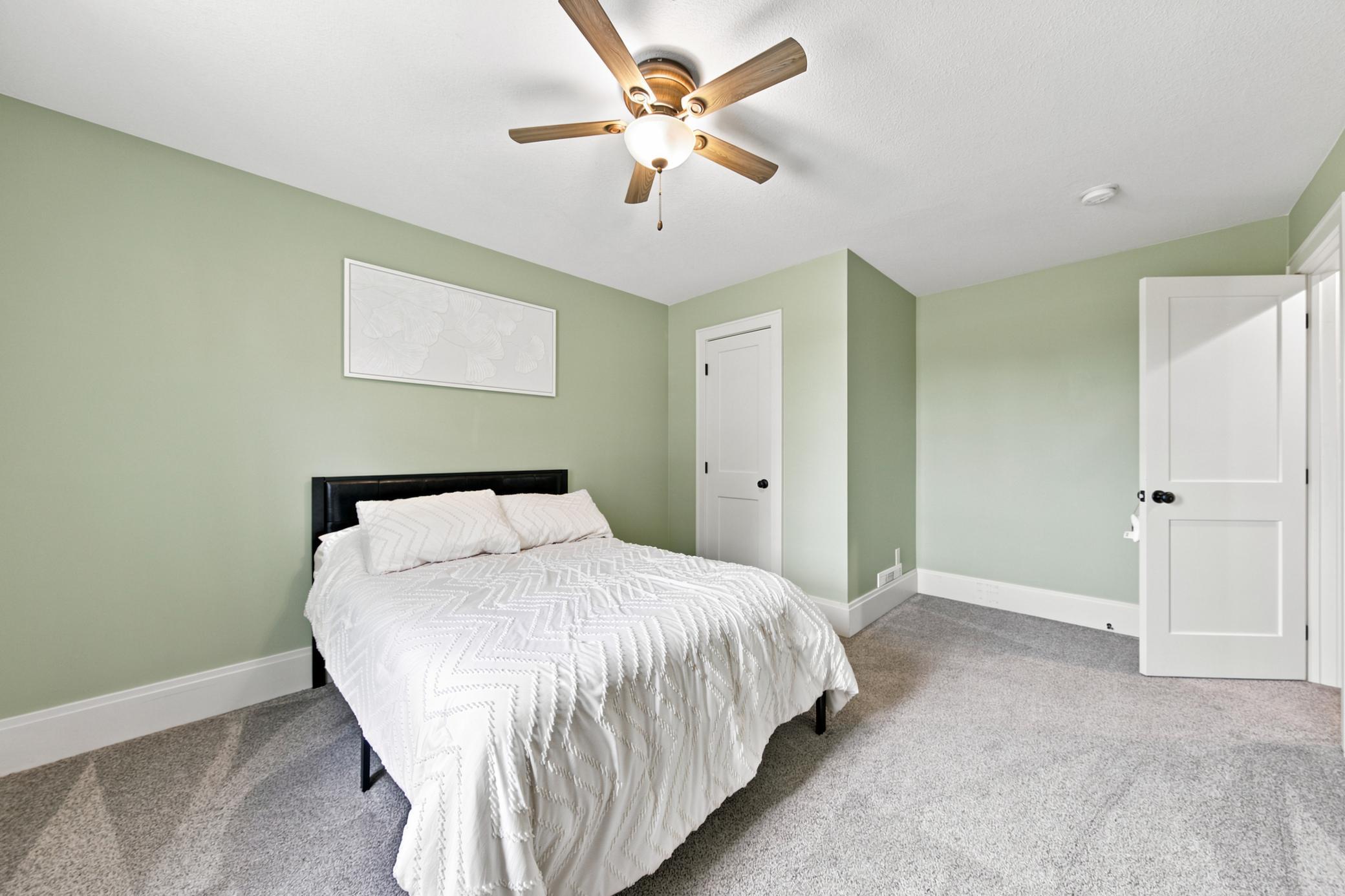 This convenient main-floor bedroom features a serene color palette, plush carpeting, and a classic wood-blade ceiling fan.