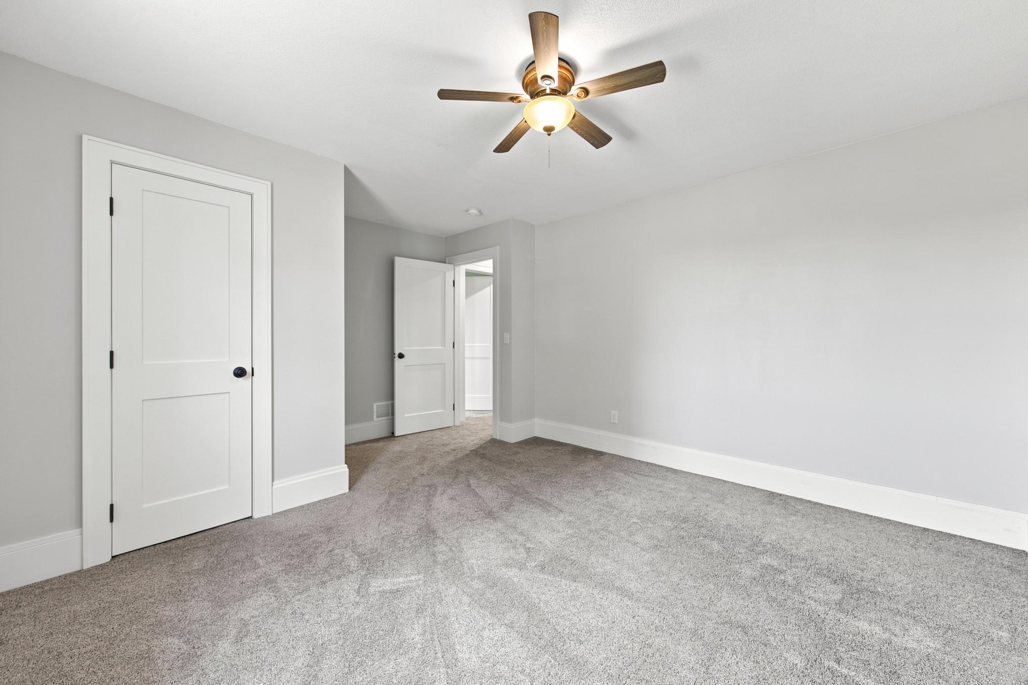 Another comfortable main-floor bedroom offers a crisp neutral color palette, plush carpeting, a classic wood-blade ceiling fan.