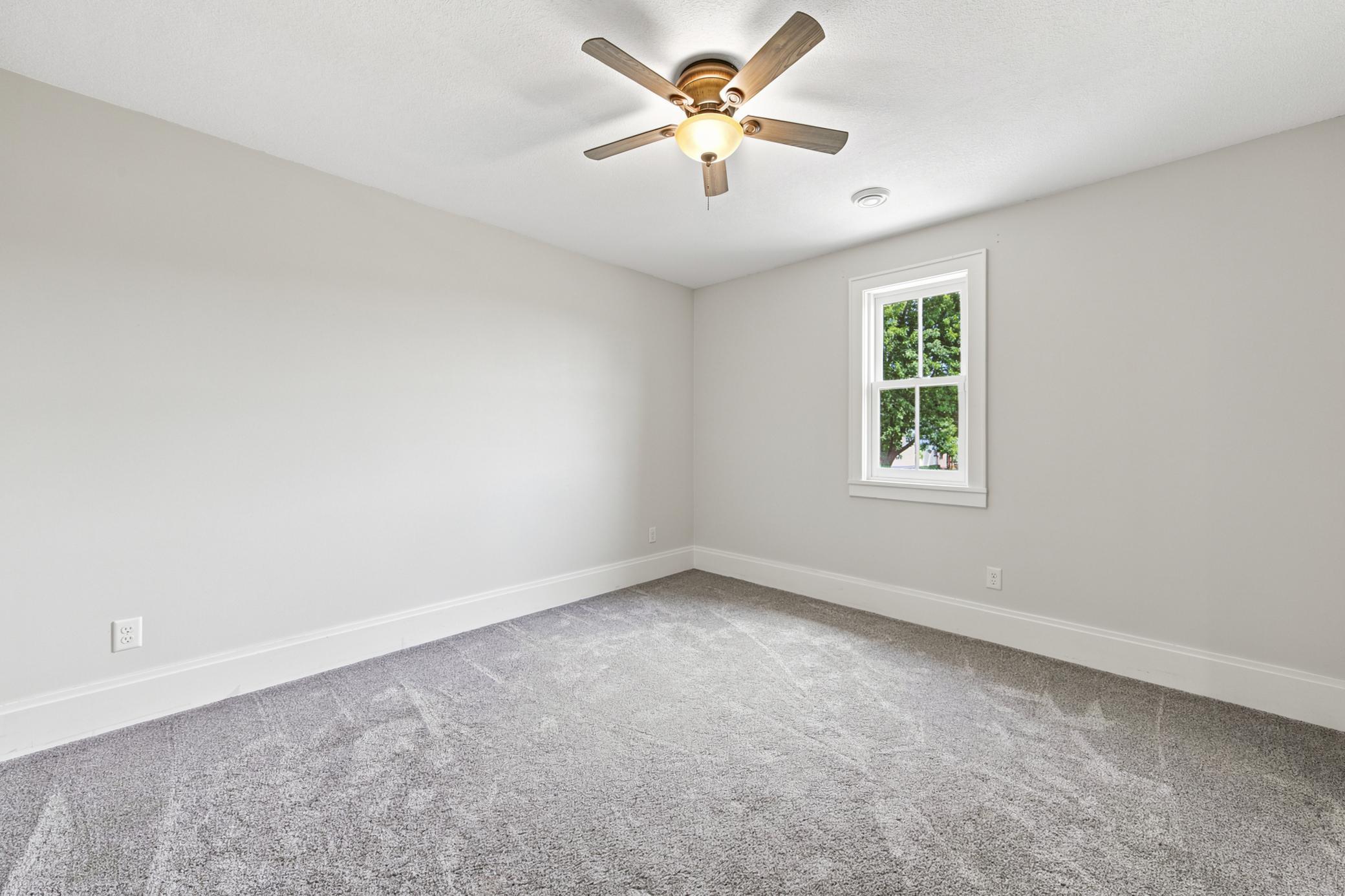 Another comfortable main-floor bedroom offers a crisp neutral color palette, plush carpeting, a classic wood-blade ceiling fan.