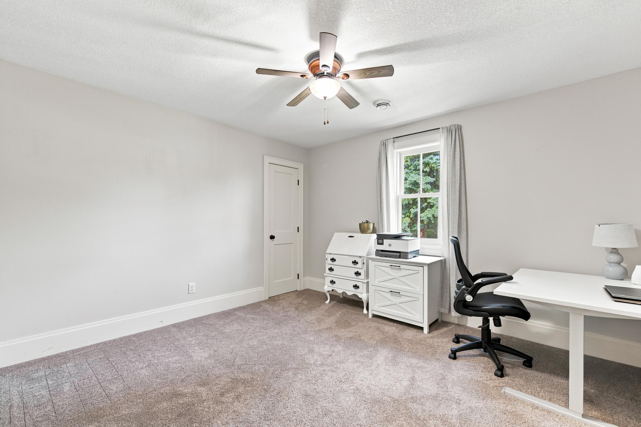 Another comfortable main-floor bedroom offers a crisp neutral color palette, plush carpeting, a classic wood-blade ceiling fan.