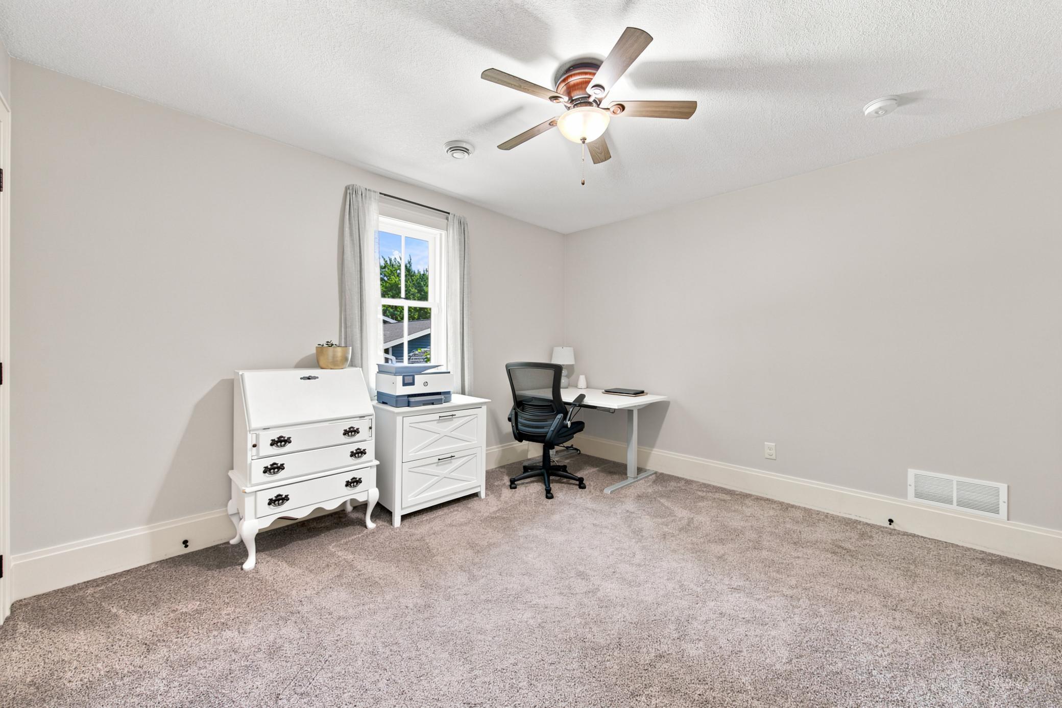 Another comfortable main-floor bedroom offers a crisp neutral color palette, plush carpeting, a classic wood-blade ceiling fan.
