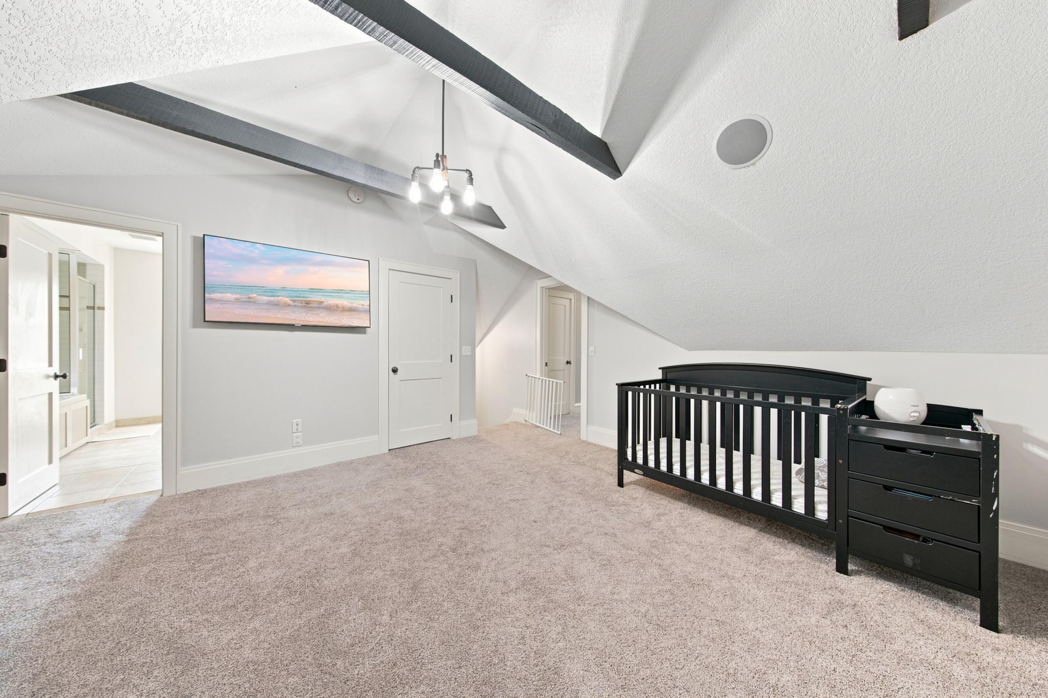 This sprawling primary suite offers an incredible bonus layout, with vaulted ceilings that connects seamlessly through elegant double doors to a private nursery or sitting room accented by rustic exposed beams.