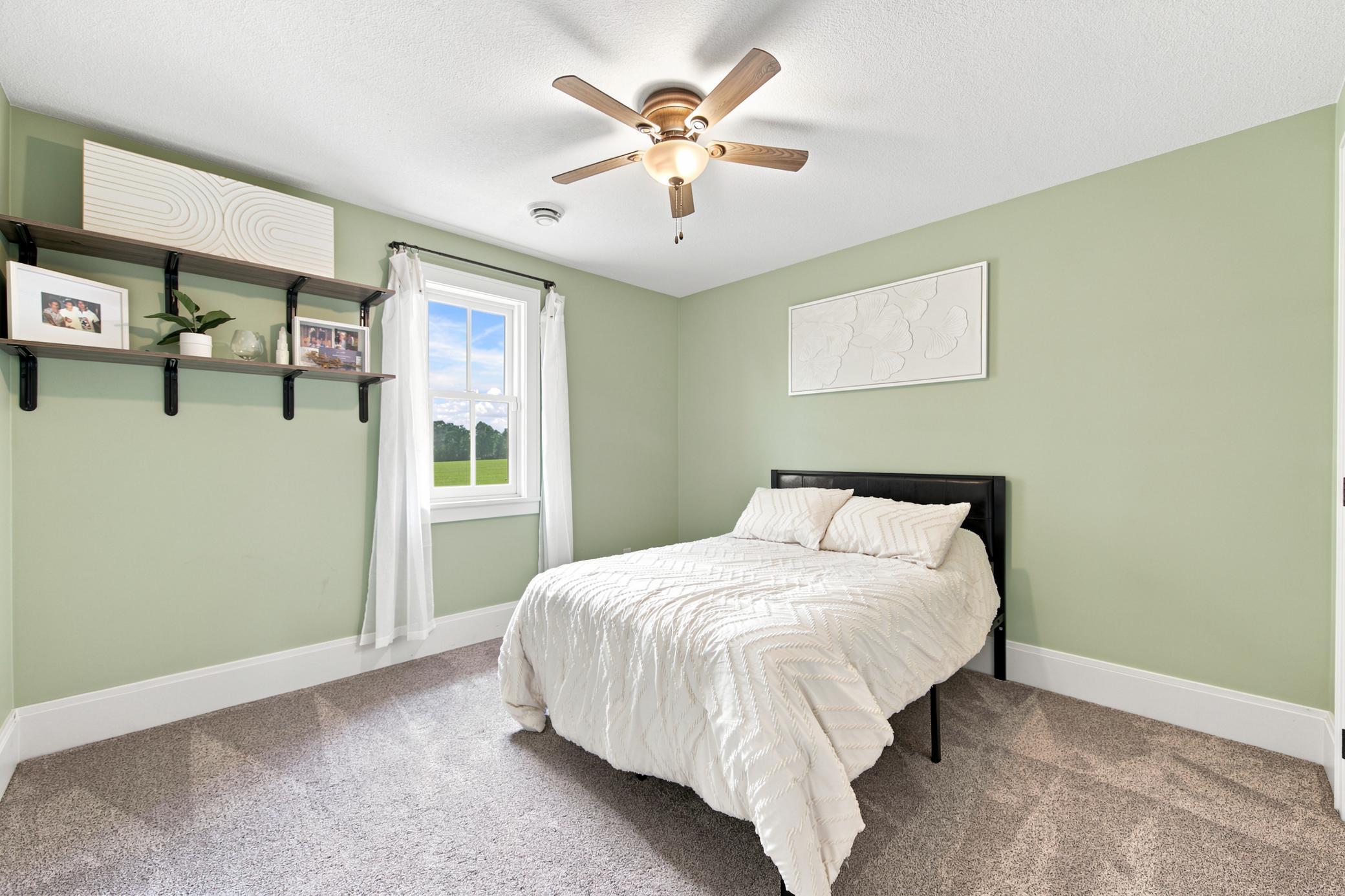 This convenient main-floor bedroom features a serene color palette, plush carpeting, and a classic wood-blade ceiling fan.