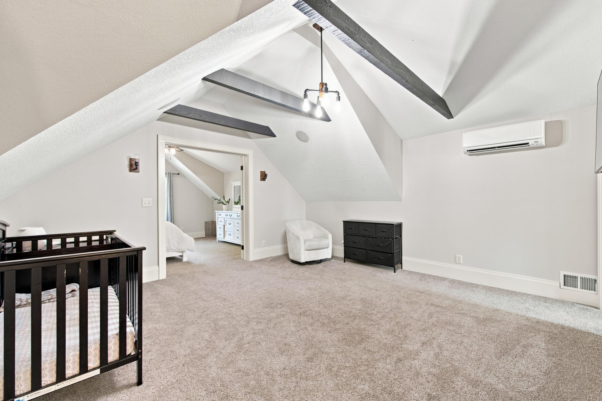 This sprawling primary suite offers an incredible bonus layout, with vaulted ceilings that connects seamlessly through elegant double doors to a private nursery or sitting room accented by rustic exposed beams.