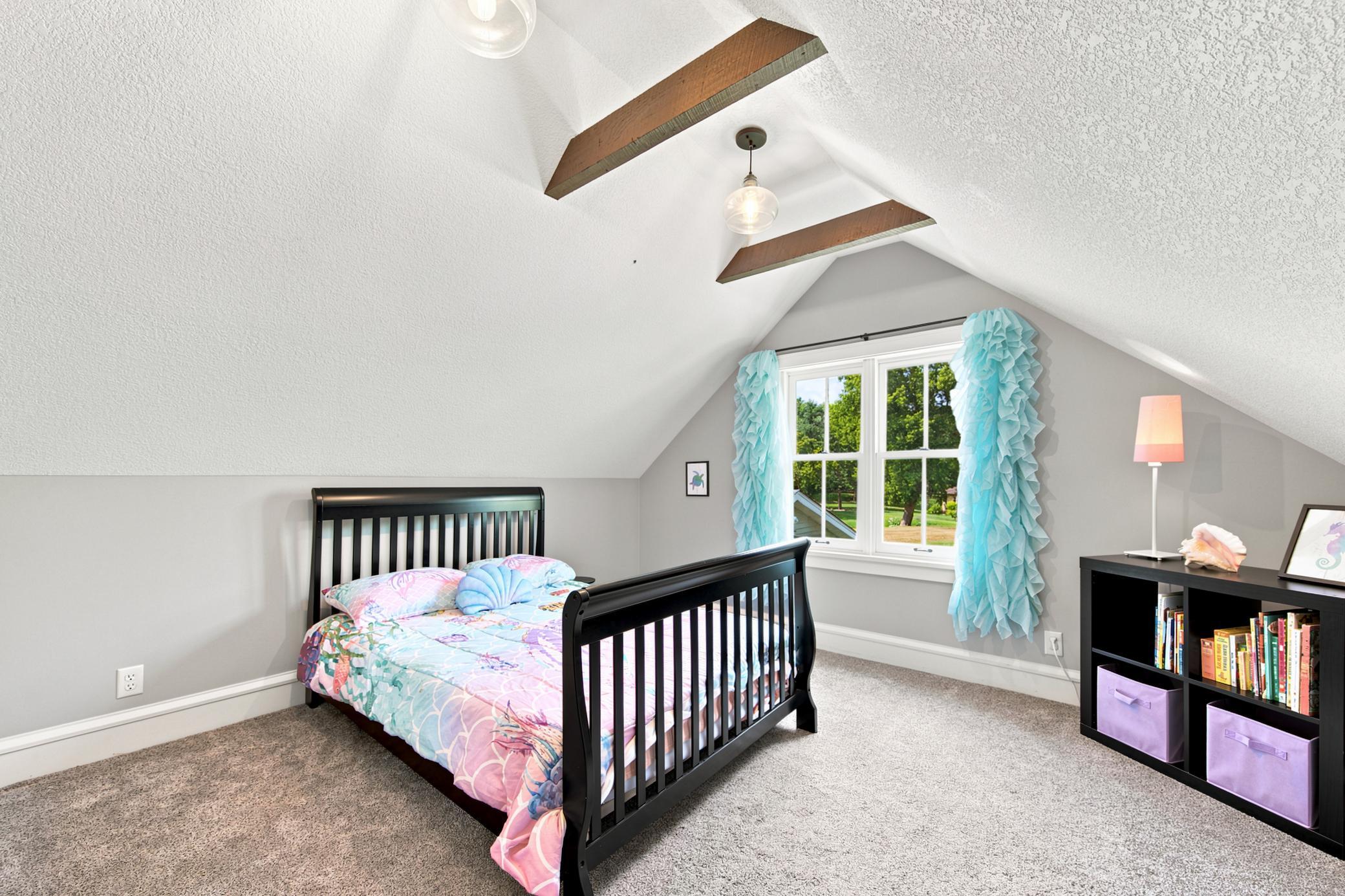This charming second bedroom connects directly to the flexible bonus space as well and features a dramatic vaulted ceiling with rustic wood beams, plush carpeting, and a bright window with scenic views.