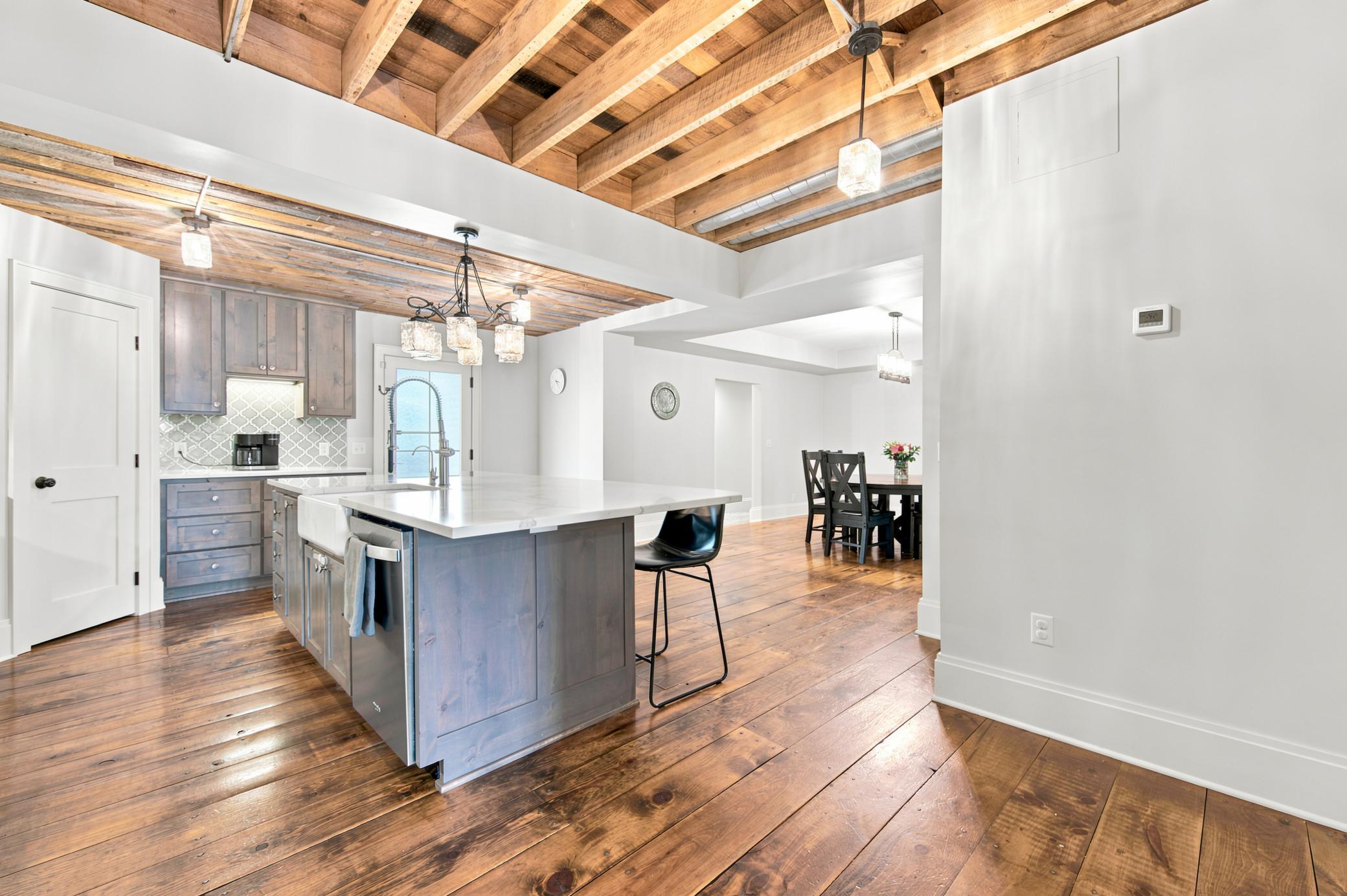 This gourmet kitchen boasts high-end stainless steel appliances, premium quartz countertops with a farmhouse sink, custom cabinetry, and dramatic exposed wood-beam ceilings.