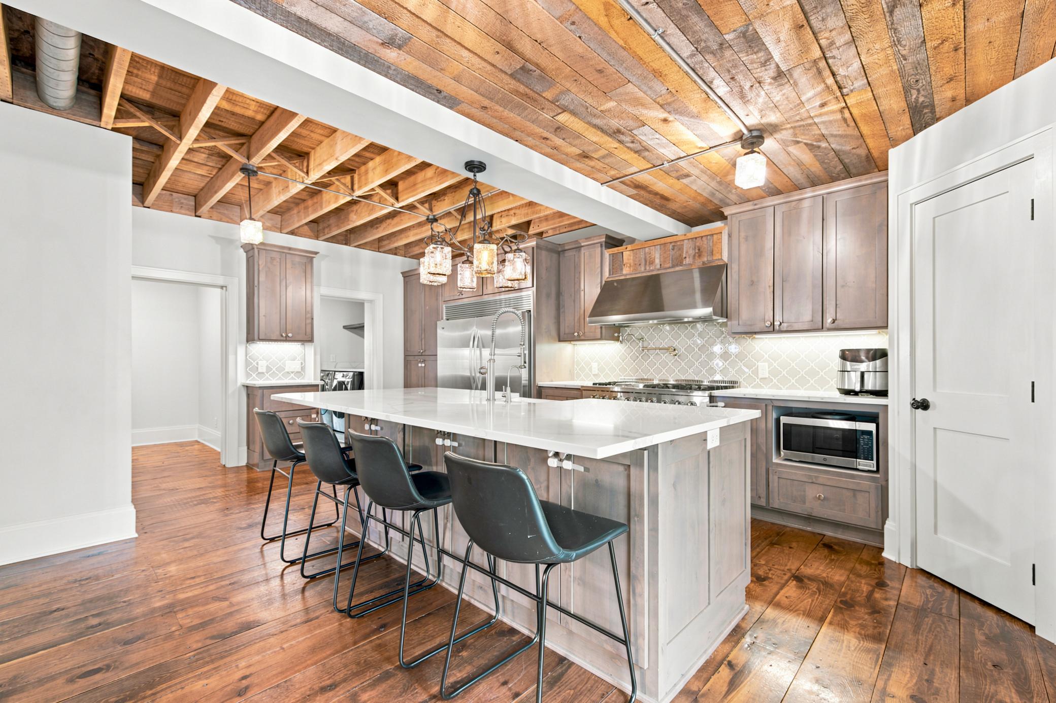 This gourmet kitchen boasts high-end stainless steel appliances, premium quartz countertops with a farmhouse sink, custom cabinetry, and dramatic exposed wood-beam ceilings.