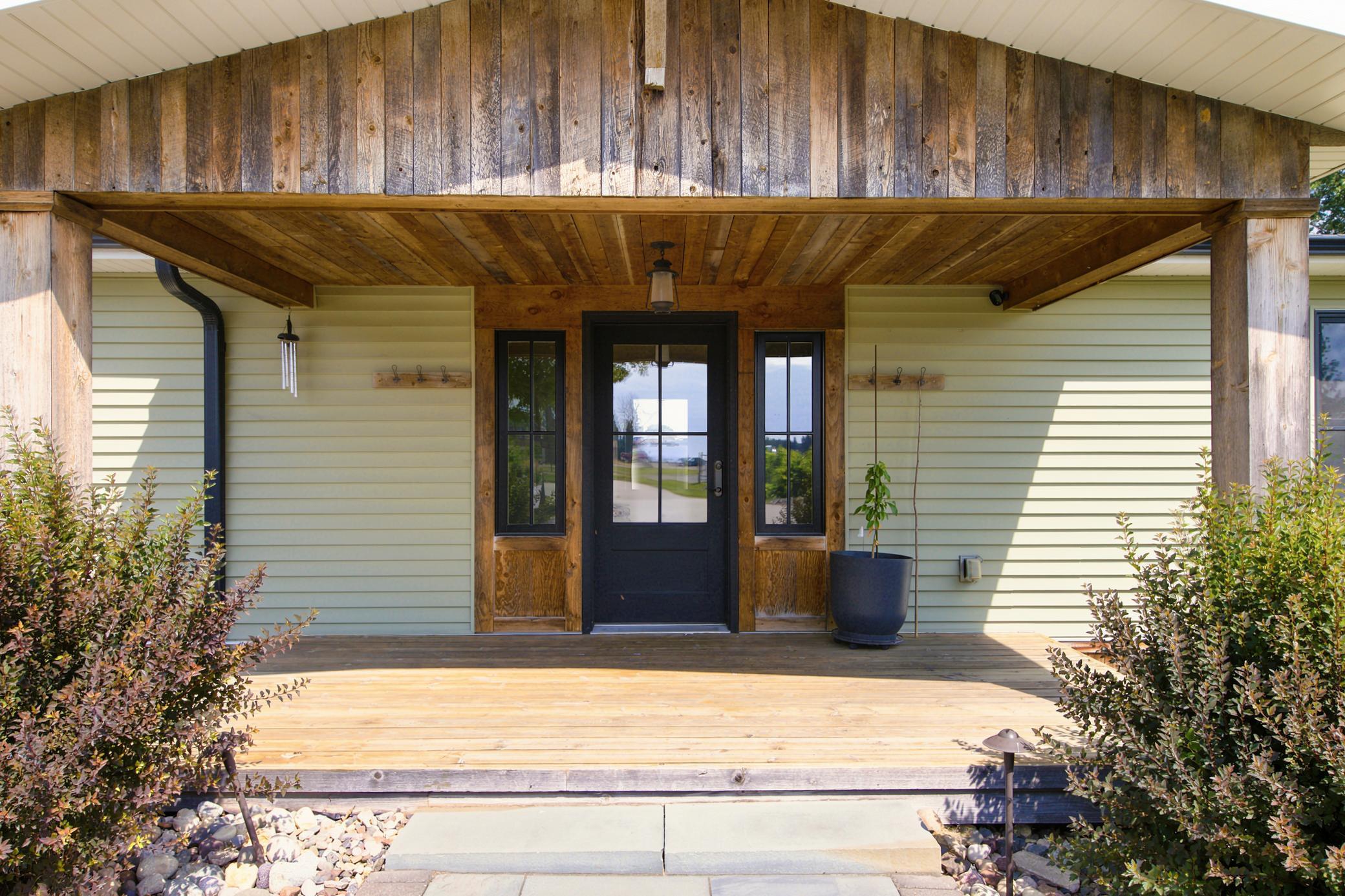 A welcoming covered front porch features warm, rustic wood accents, a modern black entry door with matching sidelights.