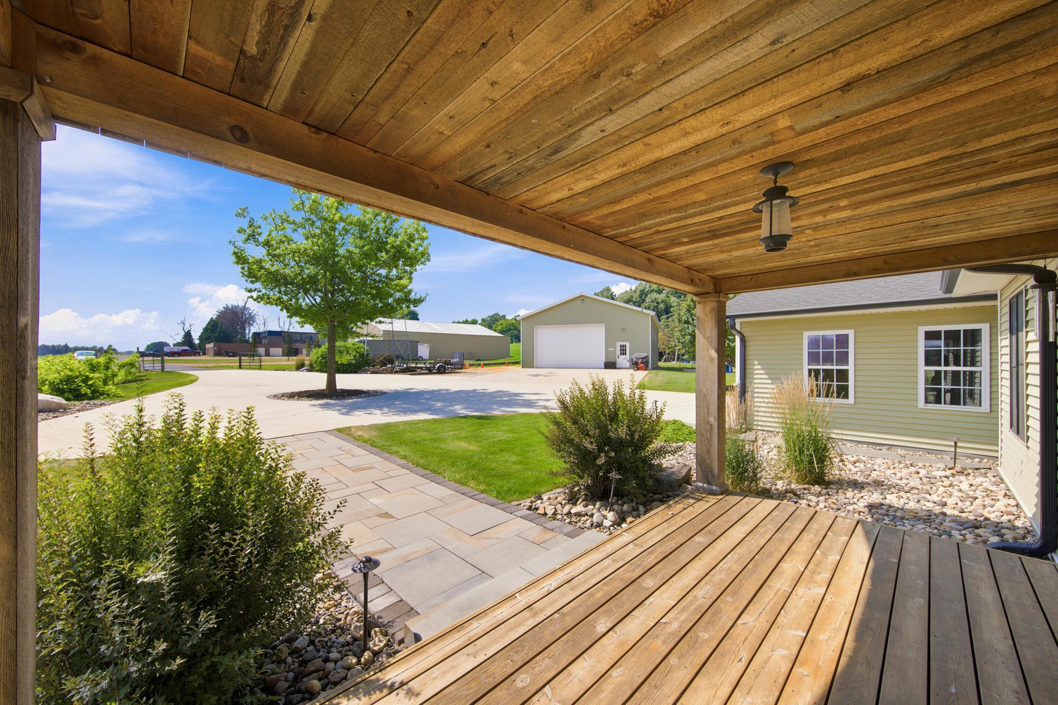 Enjoy sweeping property views from a stunning covered porch featuring a gorgeous natural wood ceiling and a manicured stone walkway.