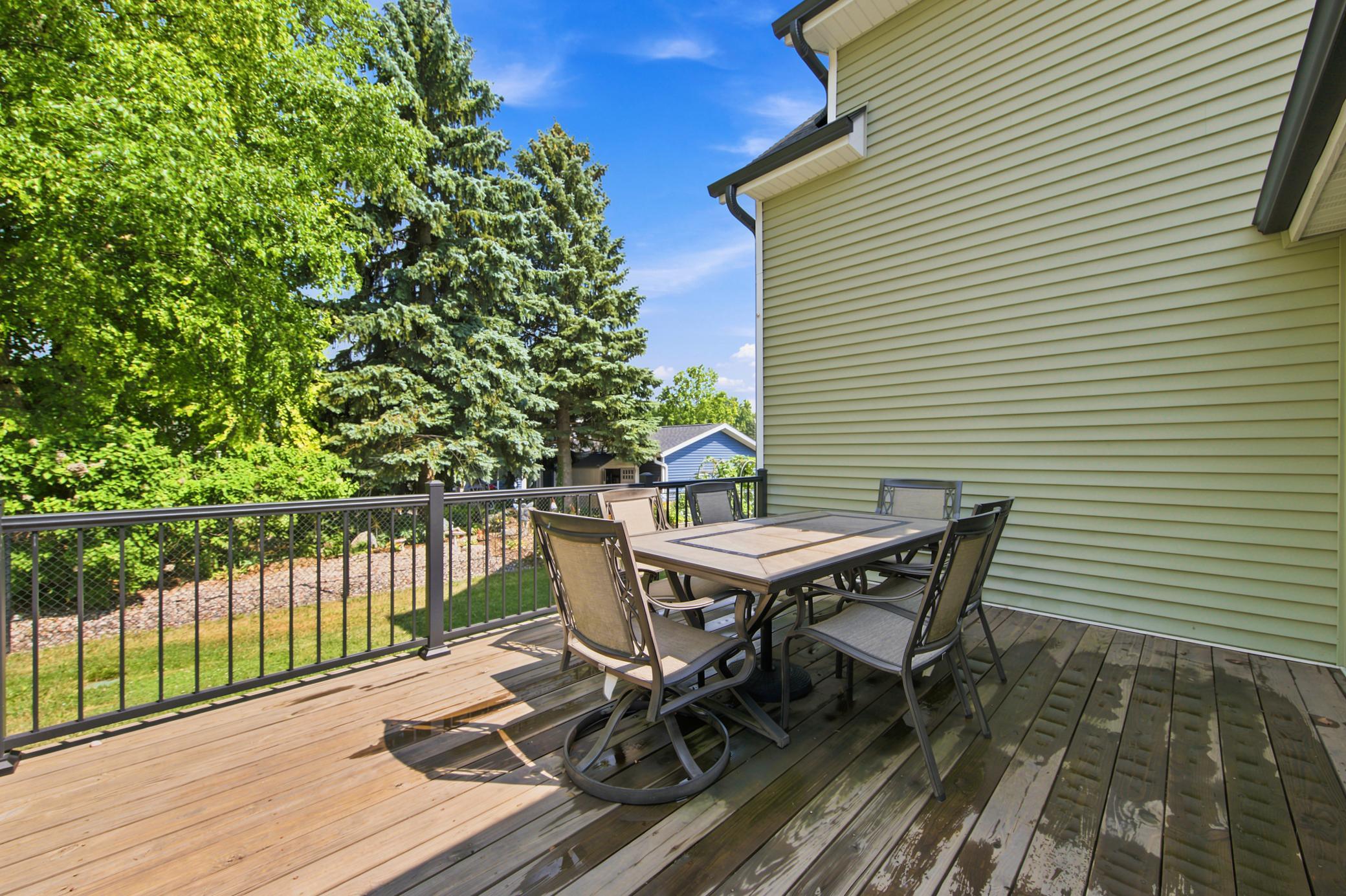 The exceptional outdoor living space features an elevated wood deck overlooking a beautifully landscape, complete with a custom stone patio, a low retaining wall, and mature privacy trees.