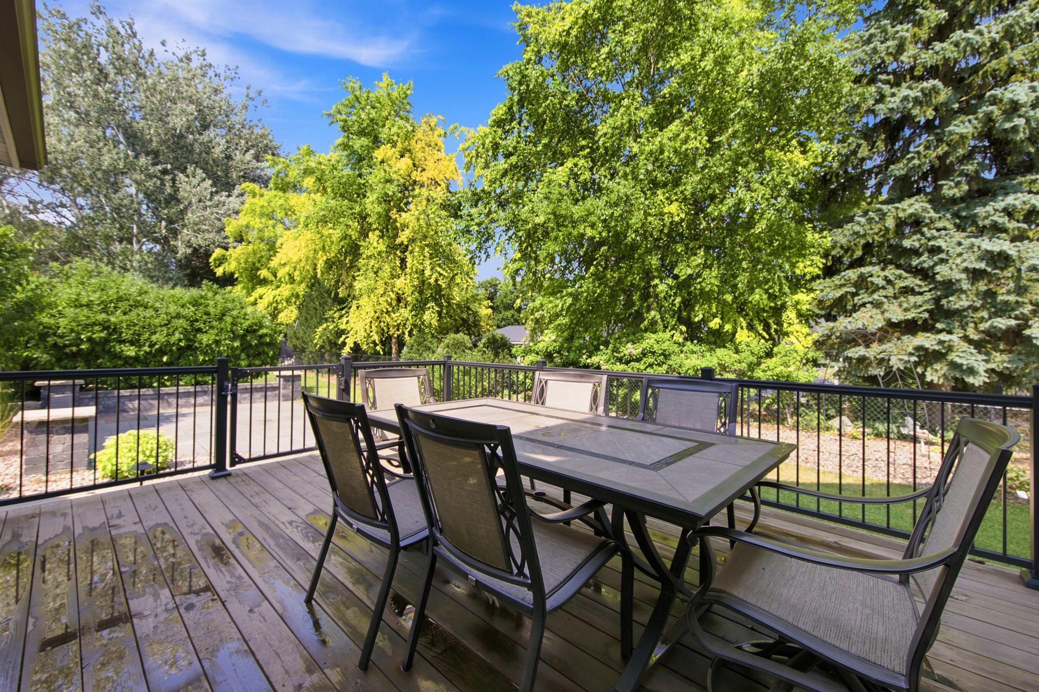 The exceptional outdoor living space features an elevated wood deck overlooking a beautifully landscape, complete with a custom stone patio, a low retaining wall, and mature privacy trees.