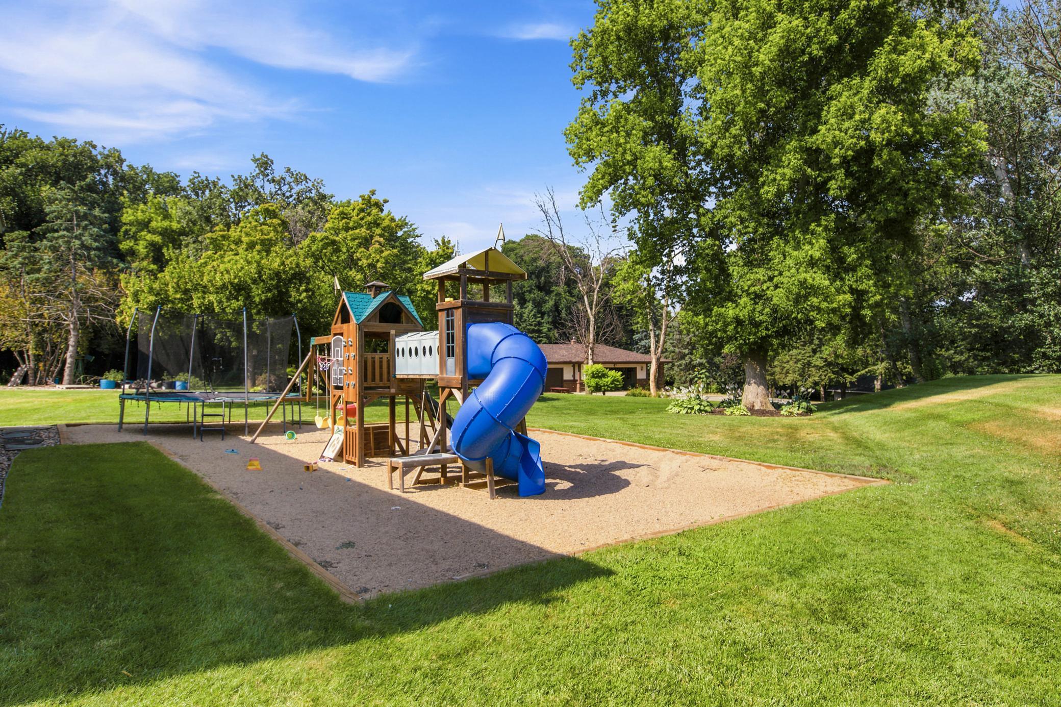 An expansive, park-like backyard offers endless outdoor entertainment with a massive open lawn and a dedicated play area featuring a large wooden playset.