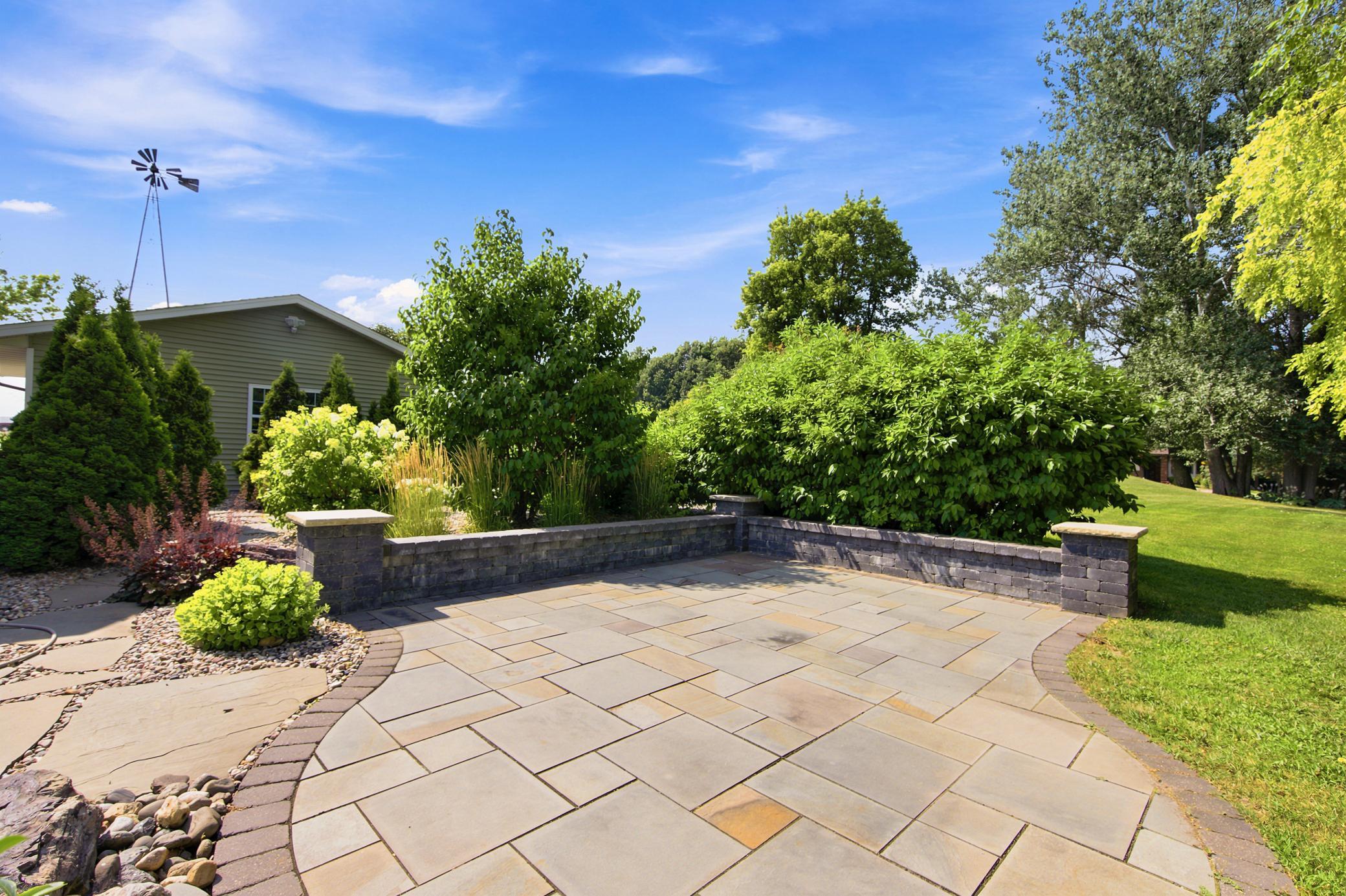 The exceptional outdoor living space features an elevated wood deck overlooking a beautifully landscape, complete with a custom stone patio, a low retaining wall, and mature privacy trees.