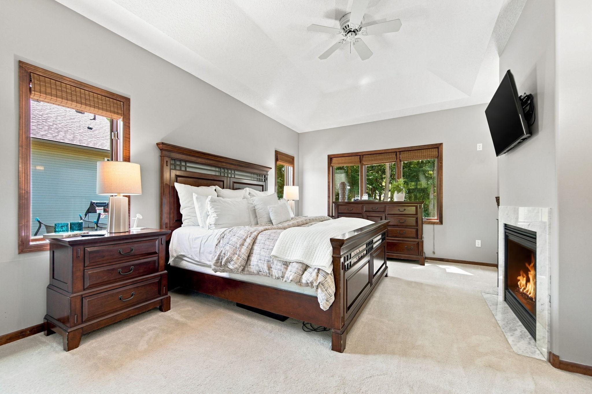 This inviting main-floor primary suite features a tray ceiling, new carpet, beautiful backyard views, generous natural light, and a cozy gas fireplace.