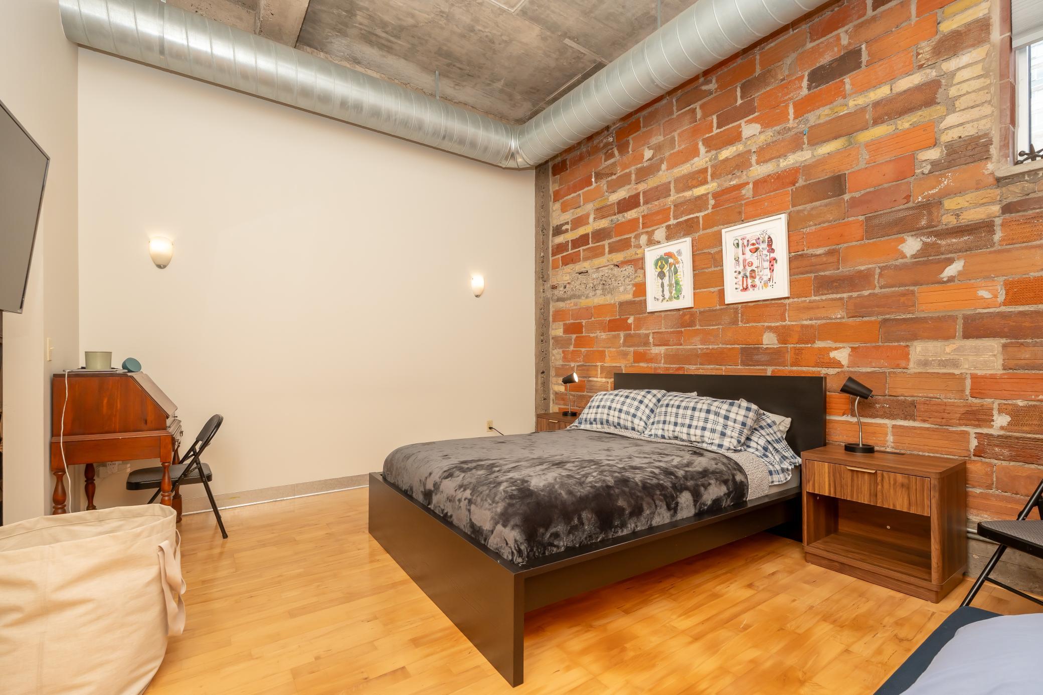 Spacious primary bedroom #1 continues with the authentic loft vibe with concrete ceilings, exposed ductwork, and an exposed brick feature wall