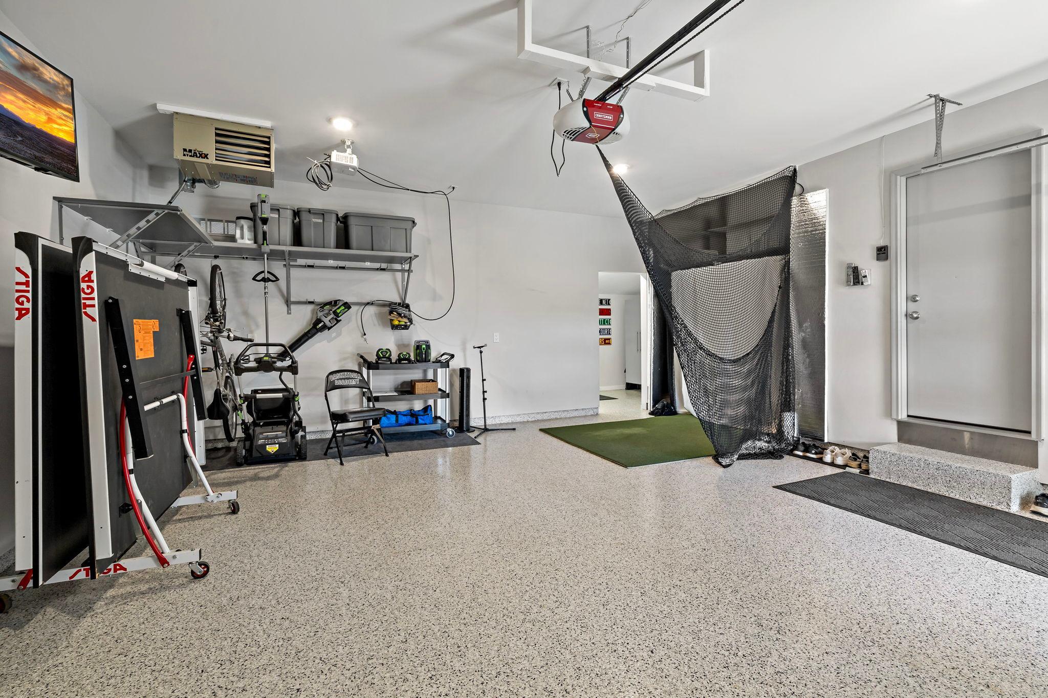 Oversized finished garage featuring an epoxy floor, gas heater, and ample space for vehicles, storage, hobbies, or a workshop