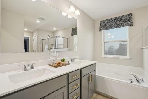 The primary suite bathroom boasts a separate shower and large soaking tub with dual sink vanity! Photo of model home, color and options will vary.