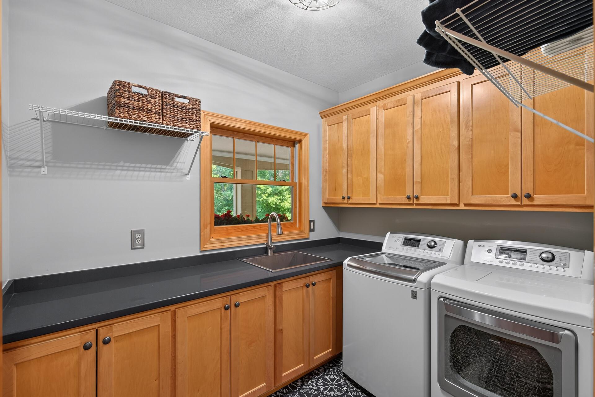 Upper and lower custom cabinetry, stone countertops, a laundry sink, and an included washer and gas dryer; this mudroom and laundry room combination redefines what a utility space can look and feel like.