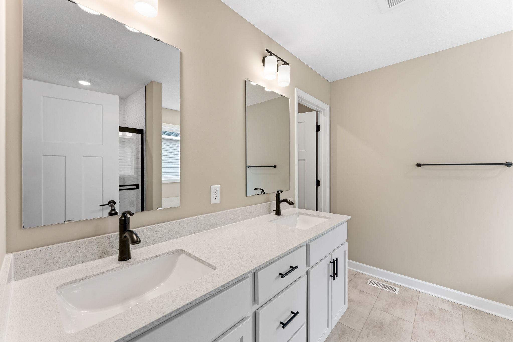 Quartz countertops, plate-glass mirrors, raised-height cabinets and Moen® Glyde faucets unite at this oversized vanity