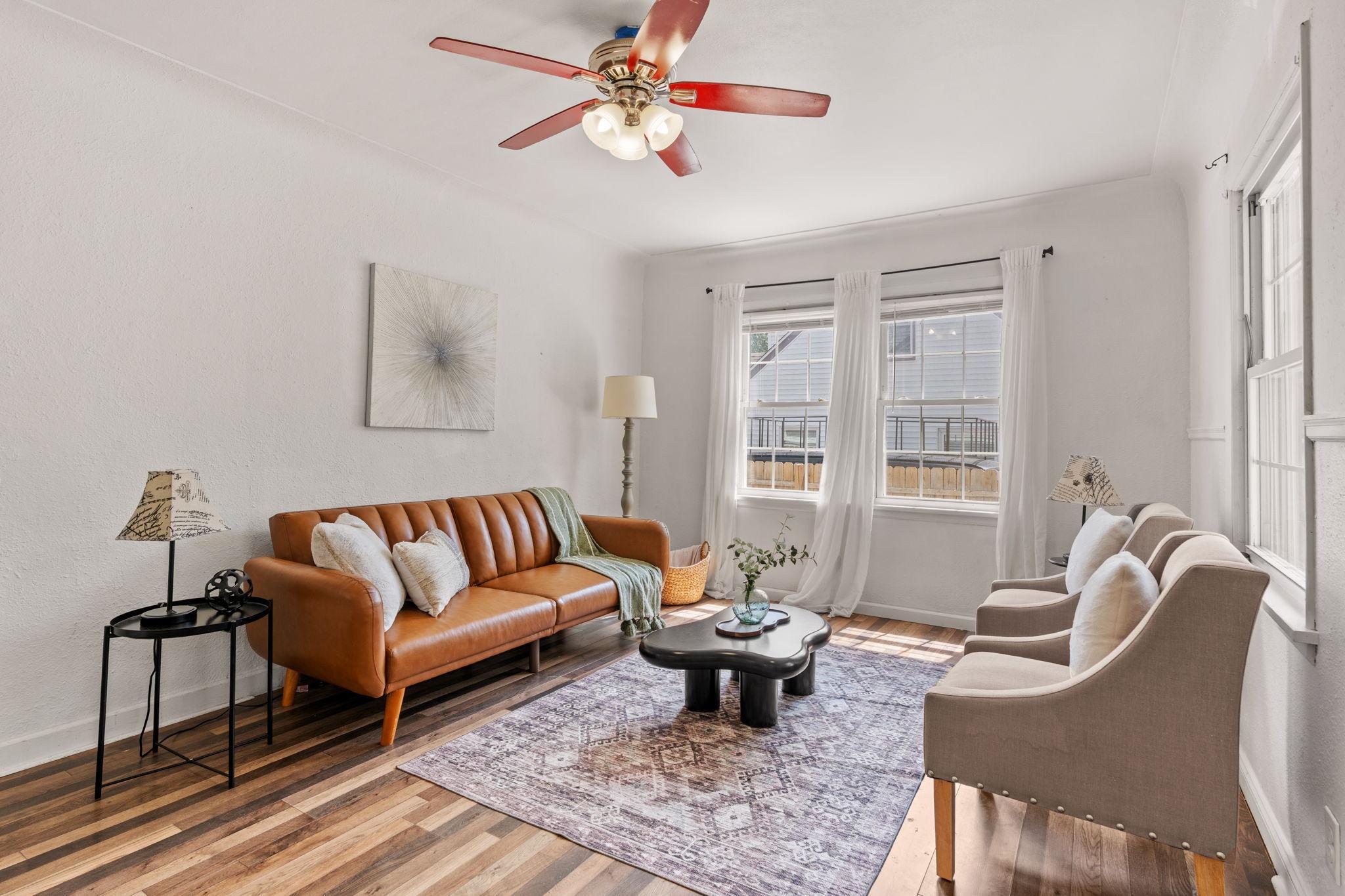 Light-filled living room with updated flooring and large front windows.