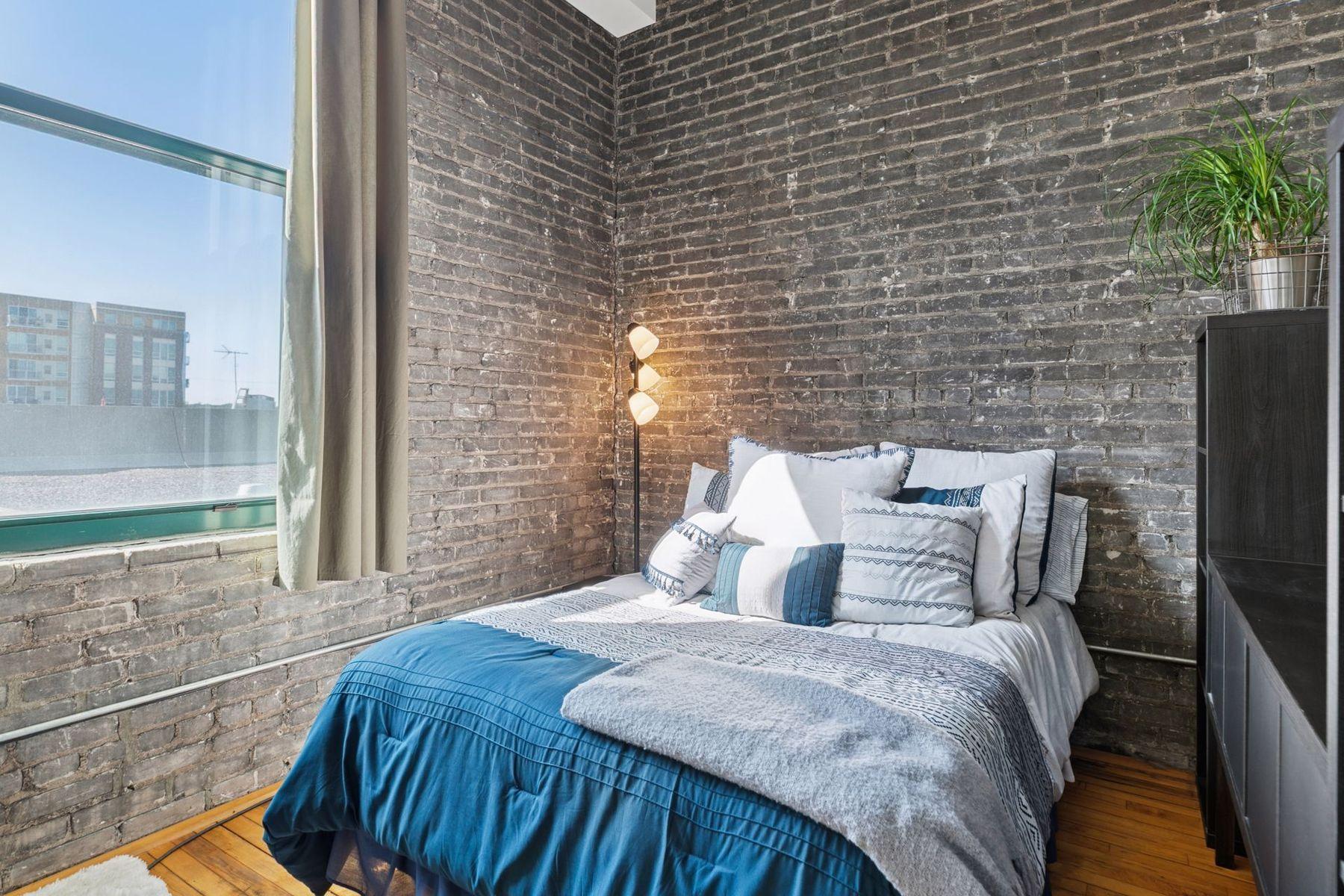 Well-defined sleeping area with brick backdrop and natural light — a smart, efficient use of space in a true urban loft.