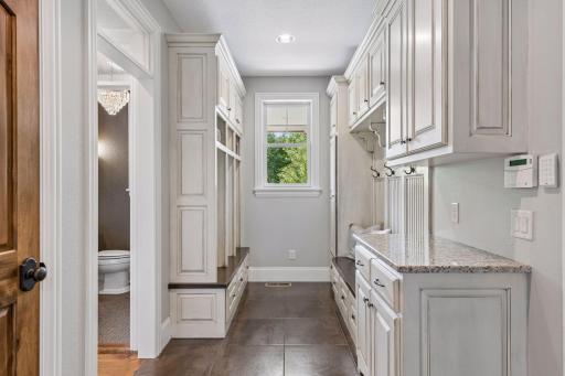 The well-designed mudroom is conveniently located off the garage and kitchen. It features custom-built cabinets, lockers, storage, tile floor a window and a large storage closet.
