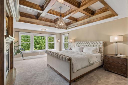 The spacious primary bedroom suite features a gorgeous wood coffered ceiling and a cozy gas fireplace with tile surround, and a wall of windows filling the room with natural light,.