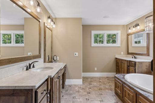 The private primary bathroom has a spa-like feel. It features dual vanities, a make-up table, ceramic tile floors, and a soaking tub with tile surround
