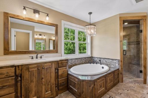 View of the private primary bathroom highlighting the knotty alder cabinets, the soaking tub with window and the walk-in shower with built-in bench.