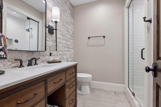 The lower level includes a beautiful 3/4 bathroom. It features a comfort-height vanity with storage, a steam shower with glass doors, subway tile and a stone floor, a decorative stone wall and a large linen closet,