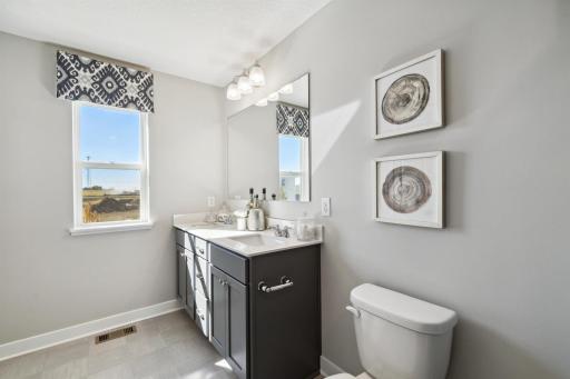 Dual vanity sinks, linen closets and window to allow natural light in primary bath. Photo of model, colors and options will vary.