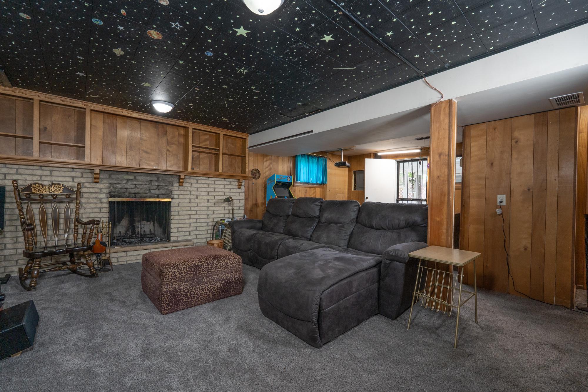 This is a lower level family room. It was being used as a theater room. It features a wood burning fireplace and behind the couch is a wet bar and that leads to the three season porch