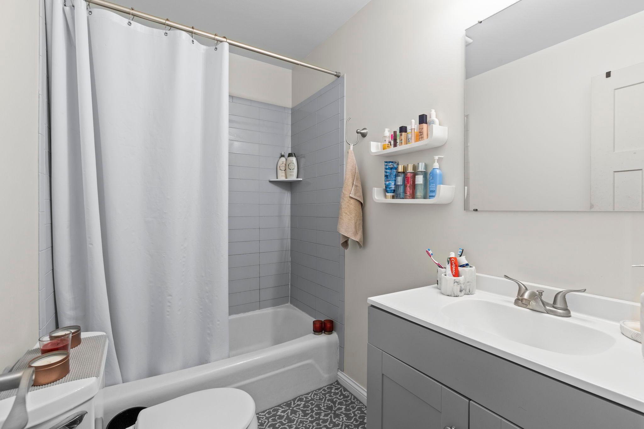 The full bathroom featuring a single vanity, tub and shower combination, and a nearby hallway linen closet for additional storage.