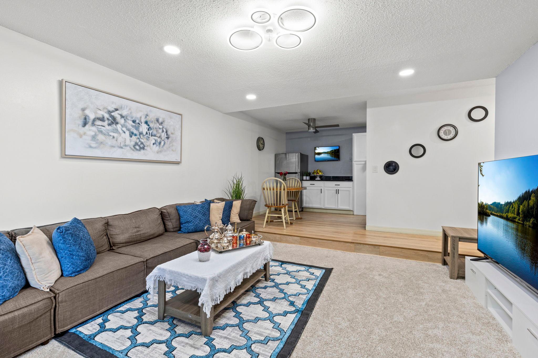 The adjacent living room features cozy carpeting, recessed lighting, a unique light fixture with a discreet fan, and access to the private balcony.