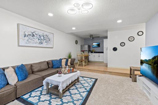 The adjacent living room features cozy carpeting, recessed lighting, a unique light fixture with a discreet fan, and access to the private balcony.