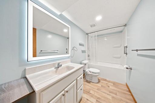 Updated lower-level full bath features modern finishes, a large vanity with illuminated mirror, and a tub/shower combination.